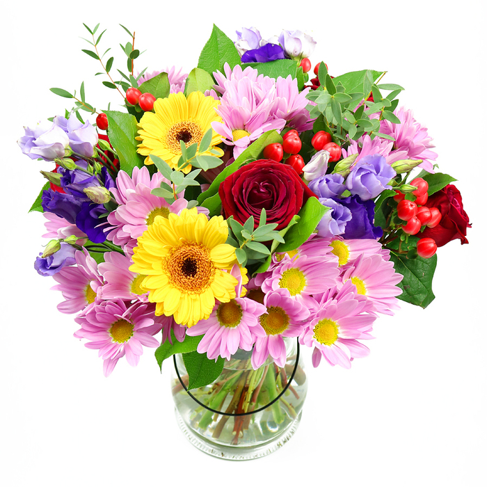 A vibrant mixed bouquet stands tall in a clear glass vase, photographed against a smooth white background that lets its colours glow as if under soft skylight above White City rooftops. In the centre of the arrangement, lush deep red roses open in tight, velvety spirals, creating a rich, romantic heart. Close beside them, two radiant yellow gerbera daisies with dark brown-orange centres bring a burst of sunshine, their bold, symmetrical petals lending the design a joyful, confident feel. Surrounding these focal blooms are abundant clusters of soft pink daisies or chrysanthemums, their many slender petals encircling small yellow centres to form a gentle pastel halo that adds volume and a friendly, approachable charm. Threaded through the pinks and yellows, graceful purple and lavender lisianthus blossoms open in bell-like shapes, the delicate folds of their petals adding cool, sophisticated notes that balance the brighter tones. Nestled discreetly between the blooms, rounded red hypericum berries offer glossy, textural accents, giving the bouquet a modern twist and a sense of playful energy. Layers of green foliage in different tones frame the flowers: broad, dark leaves that ground the design and lighter, airy sprigs that soften its edges, evoking the feeling of a well-tended garden tucked behind a White City terrace. The transparent vase reveals carefully trimmed stems and clear water, evidence of professional skill and thoughtful care from a local florist. The overall mood is bright, generous, and celebratory, perfect for birthdays, congratulations for someone starting a new role near Westfield London, or simply bringing a burst of colour to a dining table before guests arrive.