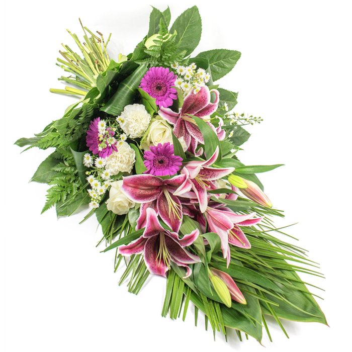 This thoughtfully arranged sympathy spray lies on a clean, white background, composed in a flowing diagonal from the top left to the bottom right, its elongated form evoking a graceful cascade that would sit beautifully in a White City chapel or crematorium. The central focus is a cluster of Stargazer lilies, their generous petals painted in deep fuchsia-pink that fades to pristine white edges, each petal marked with fine burgundy speckles that add depth and drama. Some of these lilies are fully open, their stamens extending outward, while others remain in tapered buds showing just a hint of colour at the tips. Nestled around them are vivid magenta gerbera daisies, their bold, circular heads speaking of cherished memories and love. Creamy white roses, at various stages of opening, combine with soft, ruffled white carnations to create a cushion of calm, pure tones that balance the brighter pinks. Tiny white filler flowers, reminiscent of miniature daisies, are scattered throughout, providing delicate highlights and a sense of lightness. The arrangement is backed by an abundance of foliage: broad, glossy leaves lend strength and structure, deep green fern fronds give a soft, textural edge, and long, slender leaves sweep outward and downward, accentuating the teardrop silhouette. At the upper left, the neatly bound stems suggest fresh, hand-tied craftsmanship from a nearby florist serving White City, Shepherd's Bush, and surrounding W12 streets. The overall impression is one of quiet dignity and comfort, making this spray a fitting choice for funerals, memorial services, or condolence deliveries, offering a tender, visual tribute to a life remembered.