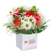 Overflowing with life and colour, this abundant bouquet shines from a pristine white gift bag, capturing the joyful energy of White City in spring. Coral and vivid crimson carnations, plush and deeply ruffled, mingle cheerfully with radiant white daisies whose centers gleam golden-green like the first morning sun over South Africa Road. Wisps of delicate white baby's breath float playfully throughout, lending an airy softness, while sturdy green leaves and glossy foliage nestle lovingly around the flowers, echoing the green spaces of Wormwood Scrubs. Hidden on the left, a handful of purple-kissed buds promise unfolding beauty. Each stem, precisely arranged in a harmonious, rounded mound, is a mark of attentive, expert design-ready to be lifted by the sturdy ribbon handles and brought to someone dear in White City, whether as a birthday surprise, an anniversary tribute, or an uplifting gesture just because. The pure white setting allows the hues and textures to glow, showcasing the artistry and warmth of fresh local florals available for delivery throughout the neighbourhood.